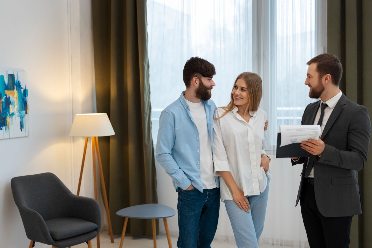 Couple in a bright room with a real estate agent, discussing papers; modern decor, relaxed atmosphere.