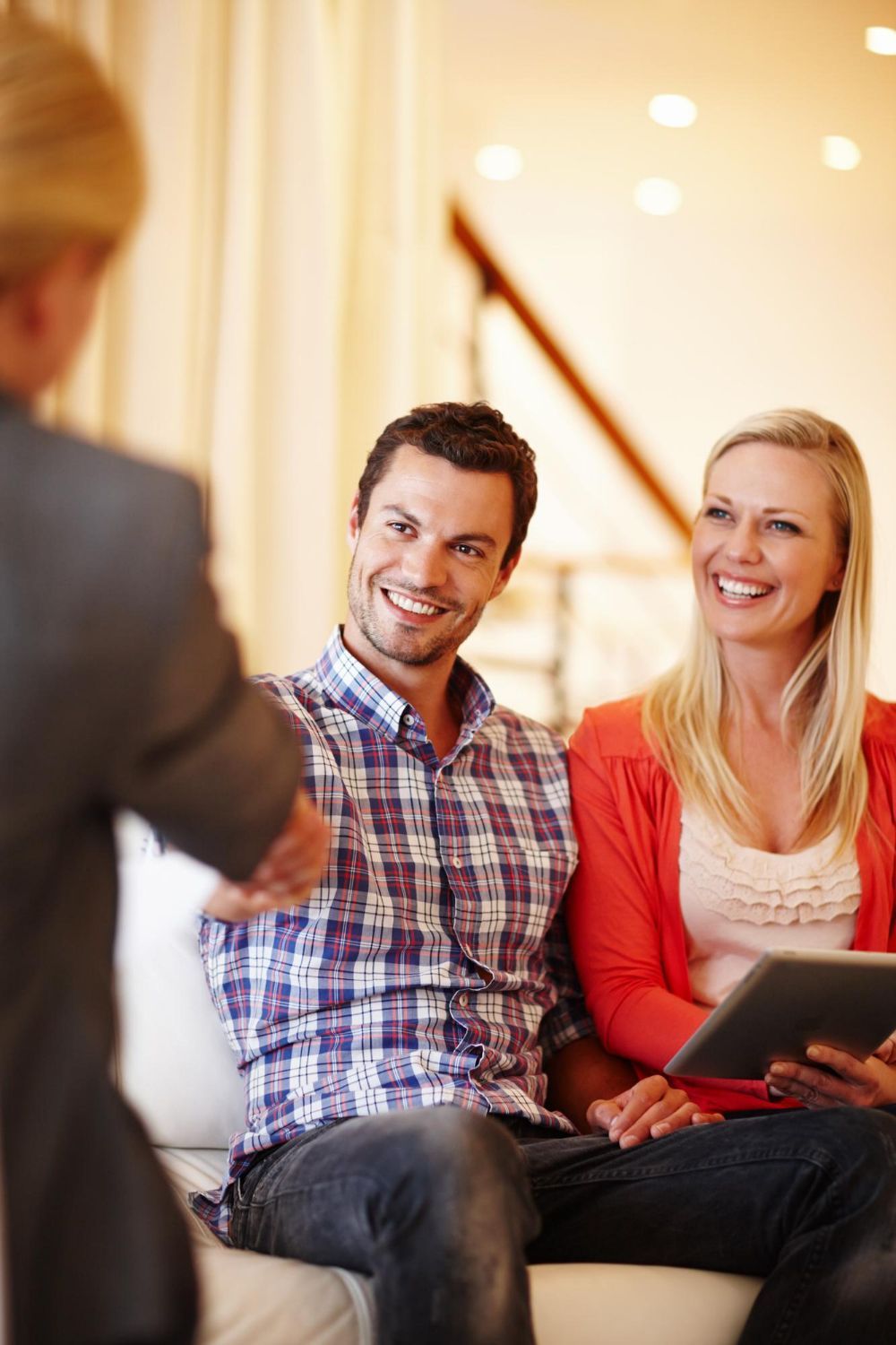 Couple on a couch smiling at a person holding documents in a living room.
