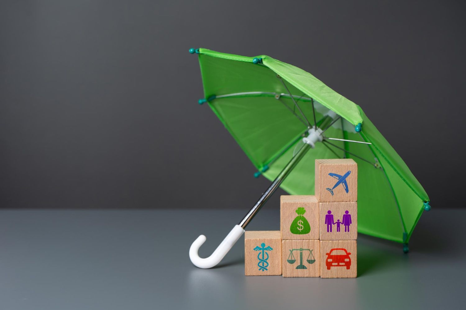 Green umbrella sheltering stacked blocks with insurance symbols.