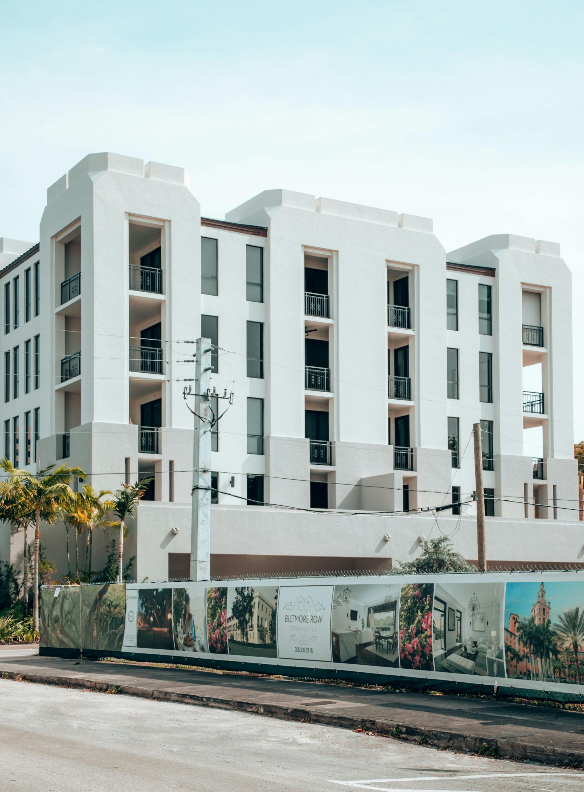White multi-story apartment building under construction, behind a construction fence with design renderings.