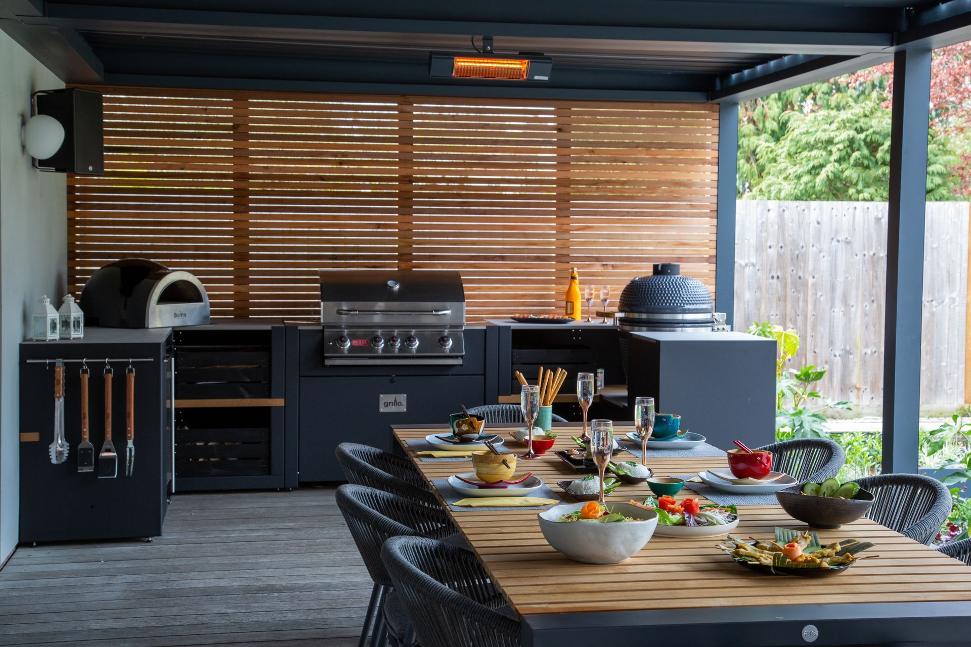 Outdoor kitchen with grill, pizza oven, dining table set for meal.