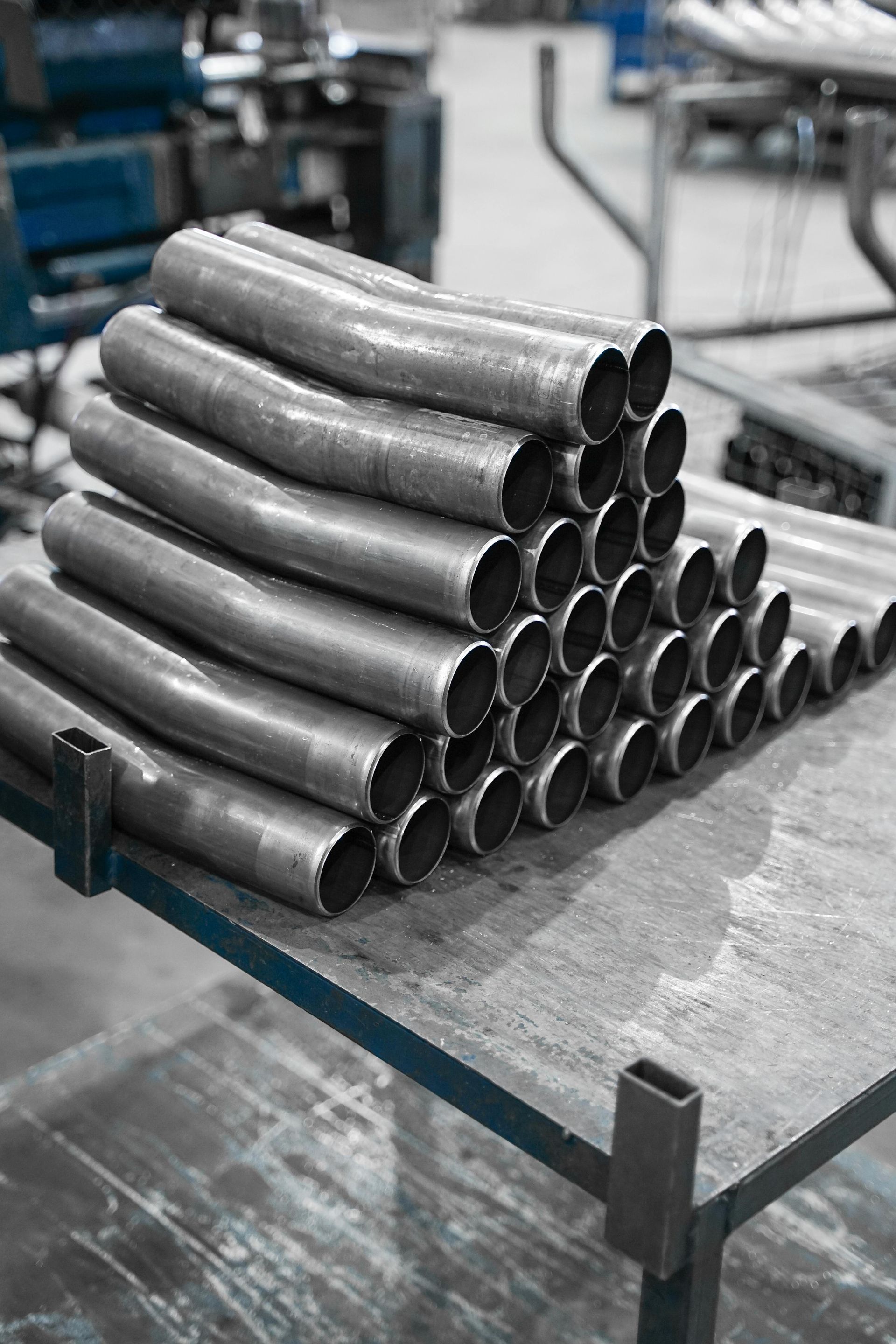 Stacked metal pipes on a factory worktable in an industrial setting.