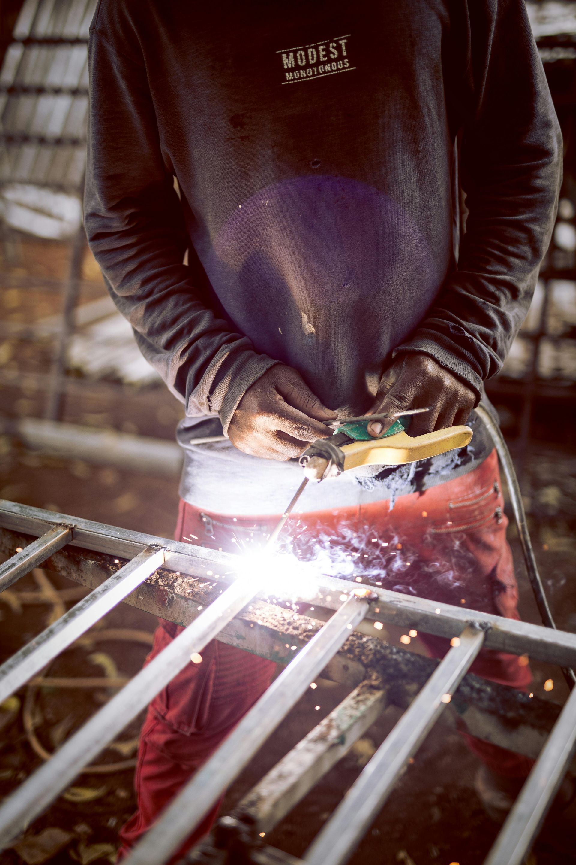 Person welding metal bars in a workshop, with bright sparks and protective gloves.