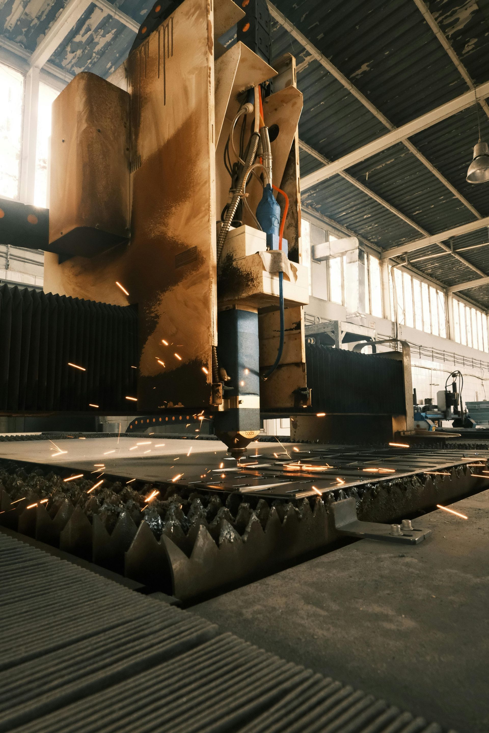 Industrial cutting machine in a factory, spraying sparks over a metal workpiece on a floor-mounted table