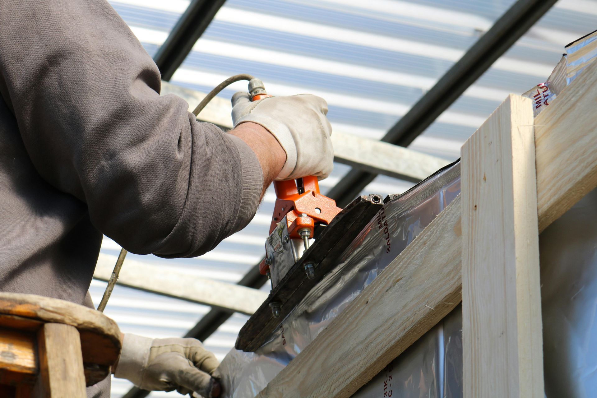Worker using a power tool on a wooden structure under a metal roof