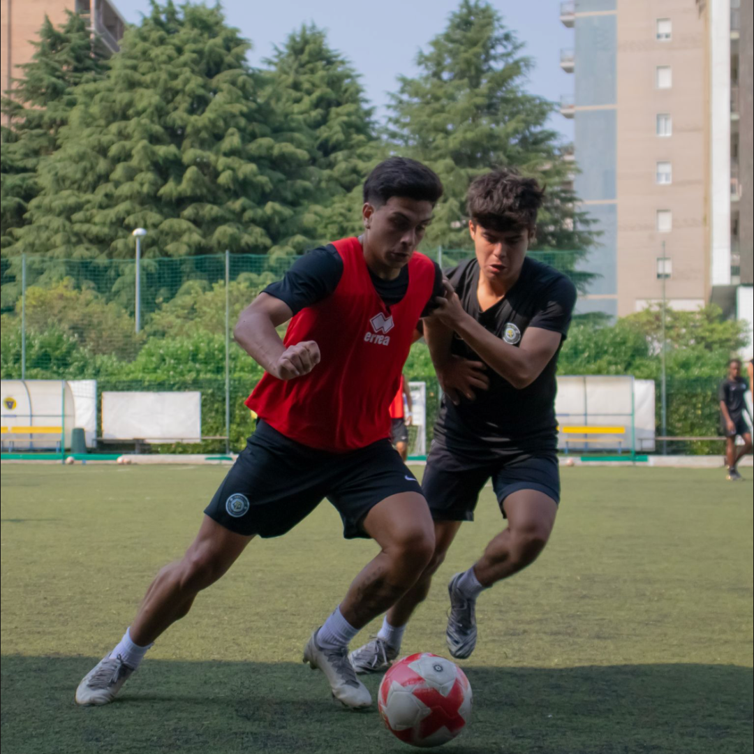 Two young men playing soccer on a green field; one dribbles the ball.