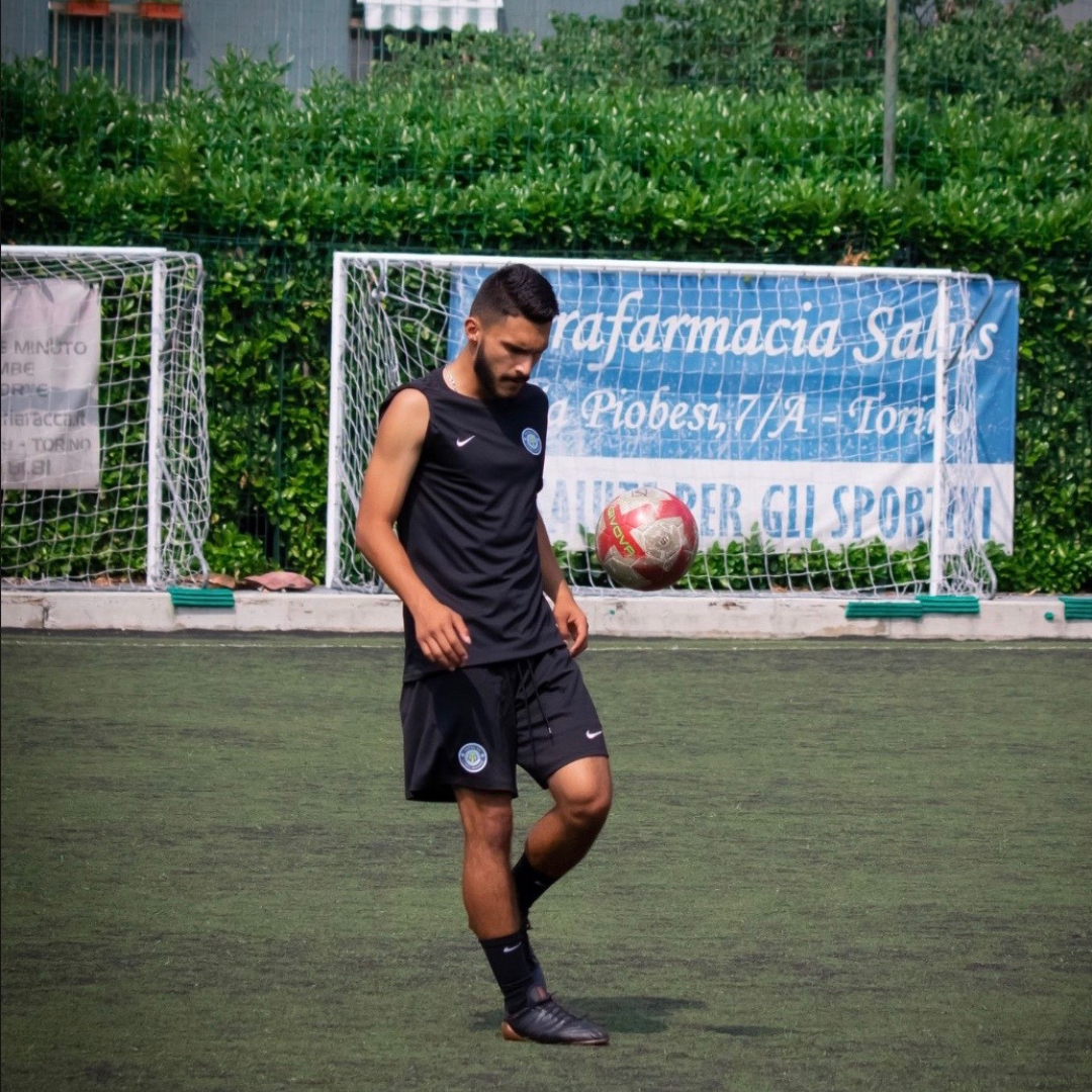 Man in black athletic wear juggling soccer ball on field.