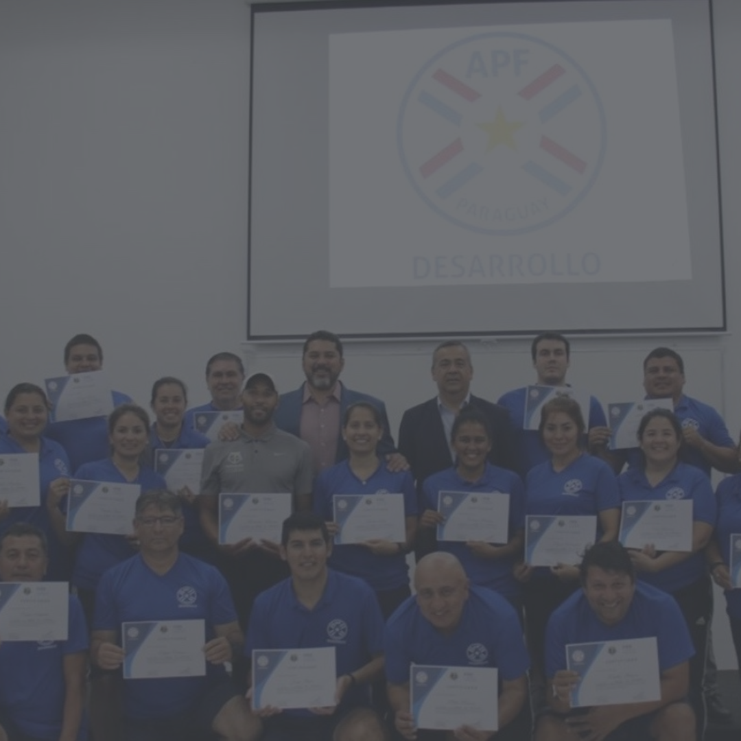 Group of people in blue shirts holding certificates, posing for photo in front of a screen with a logo.