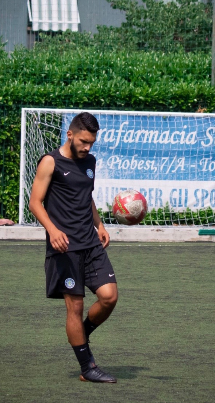 Man in black sportswear, balancing soccer ball on his foot, green field, outdoor setting.
