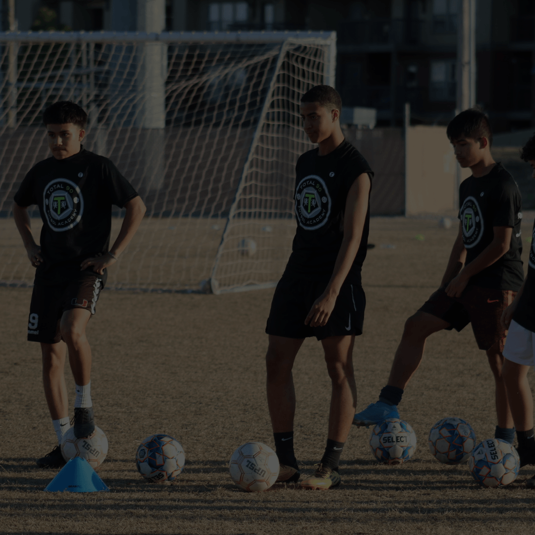 Soccer players in black shirts practicing ball control on a field near a goal.
