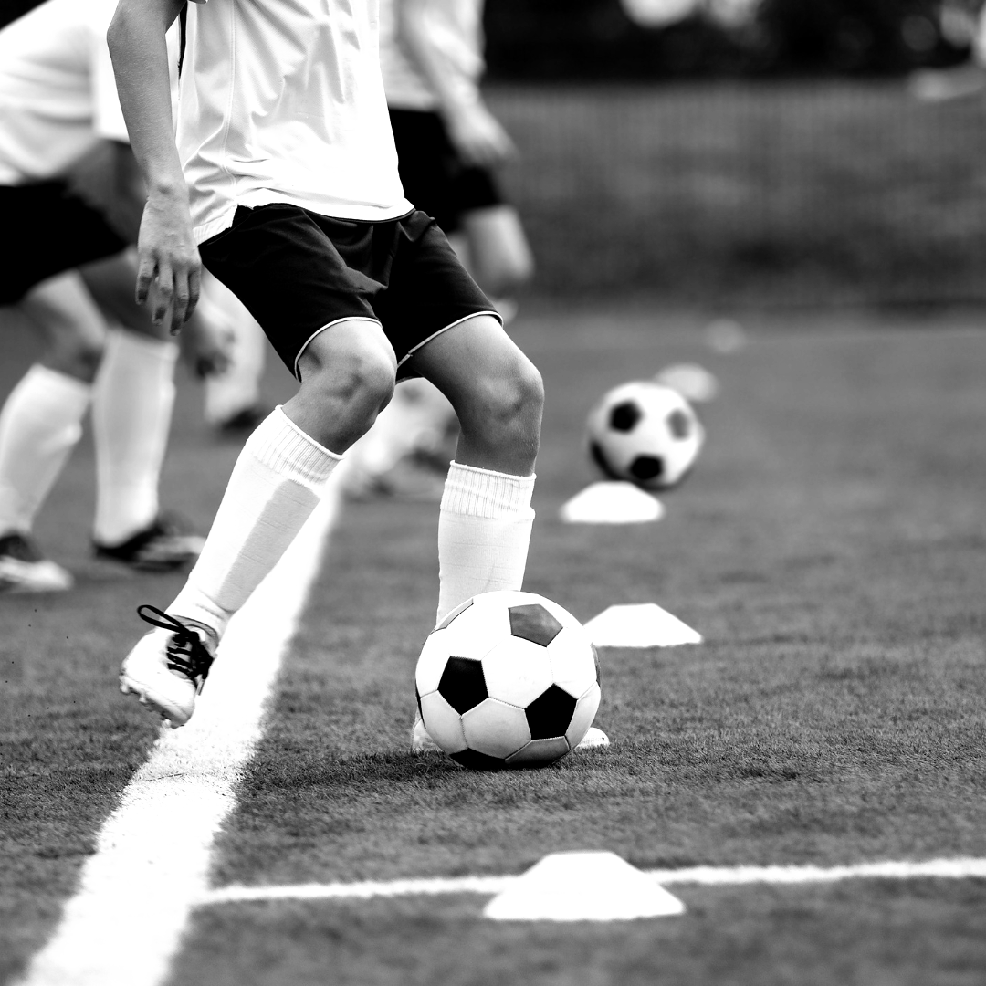 Soccer player dribbling ball along a white line on a green field during a practice drill.