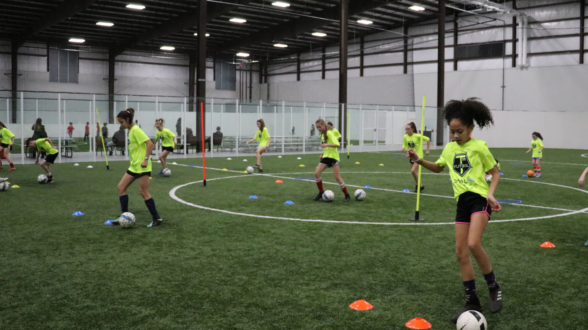 Girls in neon green soccer uniforms practice drills on indoor turf field.