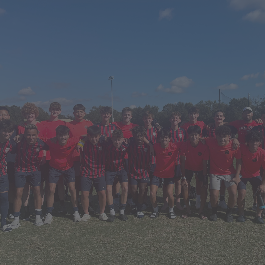 Group of people in red shirts standing on a grassy field under a blue sky.