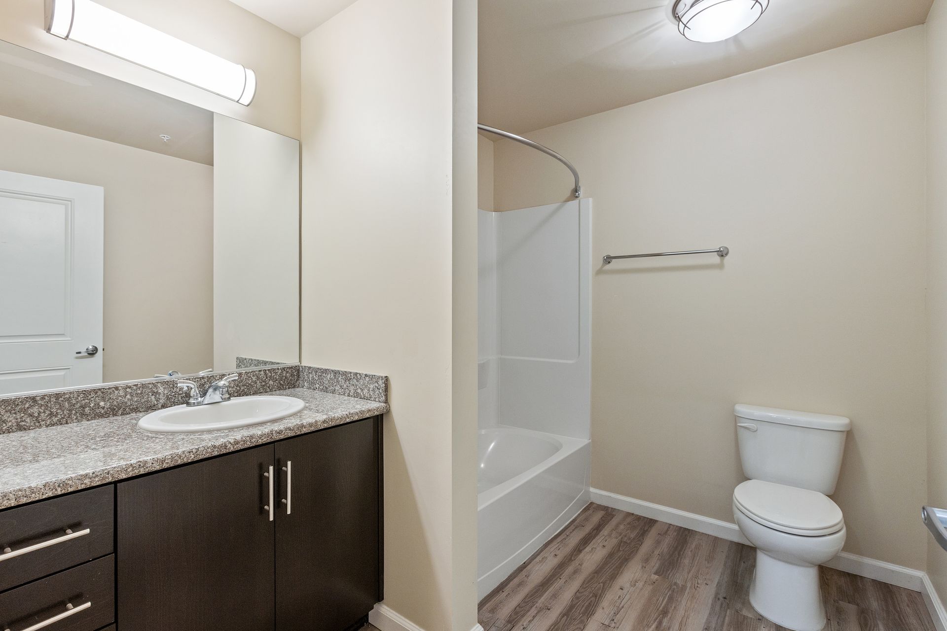Bathroom with vanity, toilet, and bathtub. Dark brown cabinets, light-colored walls, and wood-look flooring at Volare Apartments.