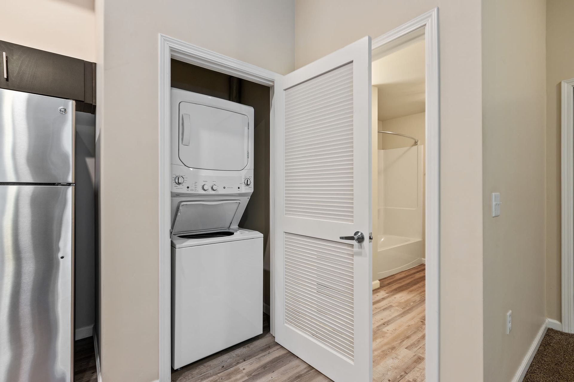 Stacked washer and dryer in a laundry closet beside a doorway to a bathroom at Volare Apartments.
