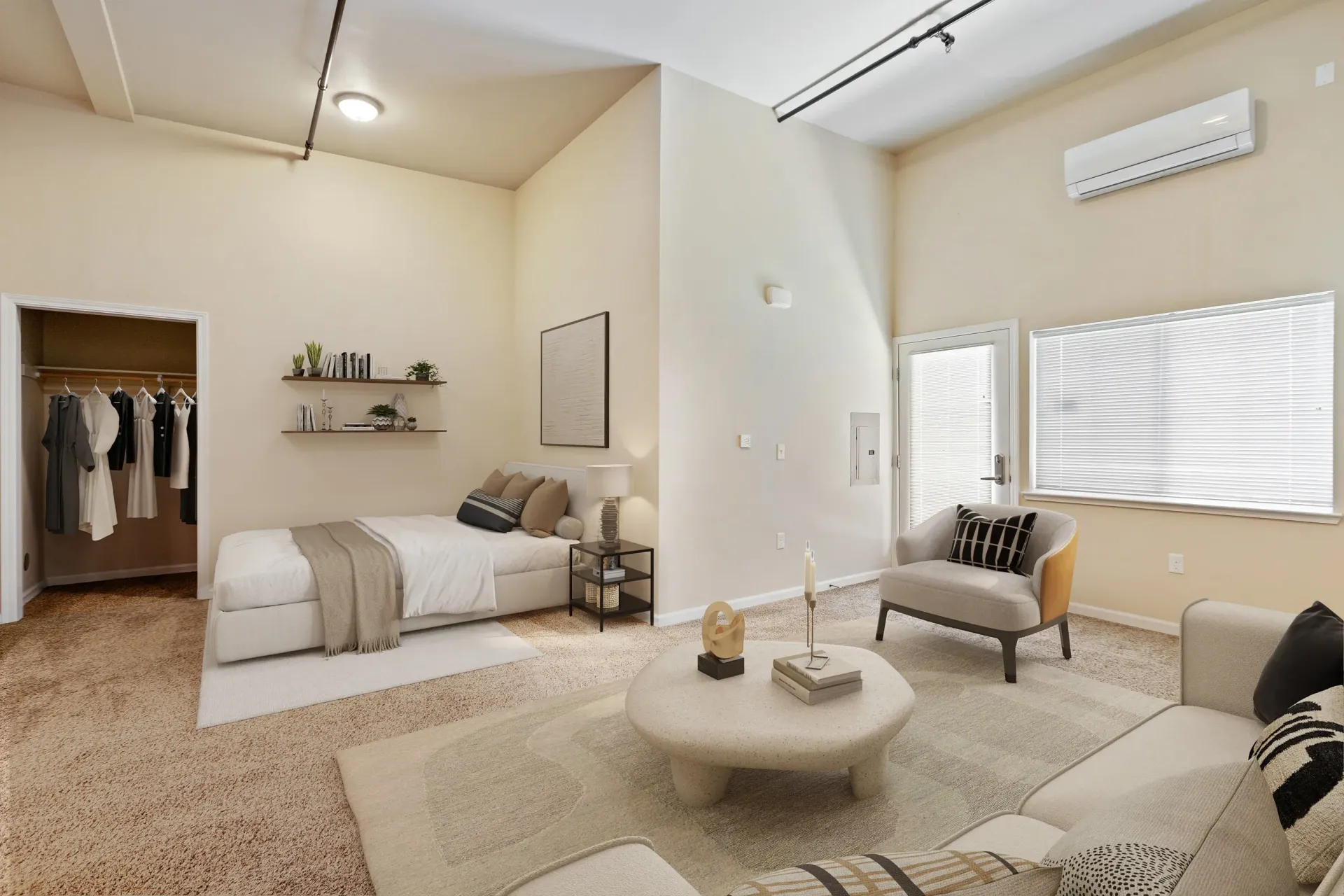 Bedroom and living area in a modern apartment with bed, sofa, coffee table, open closet, and large window at Volare Apartments.
