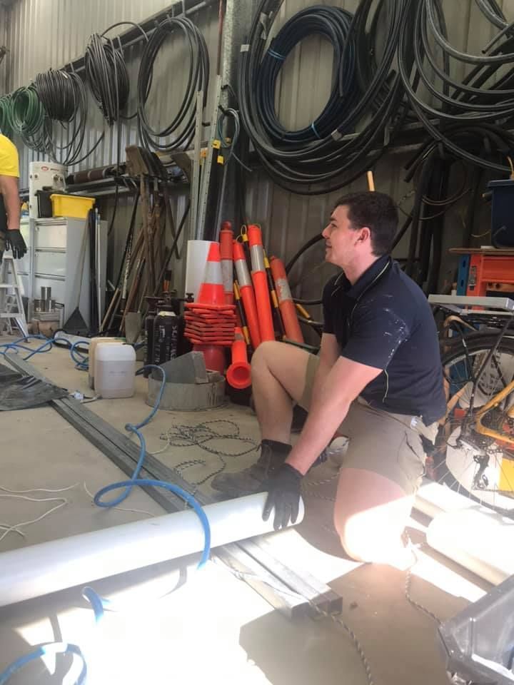 A Man is Kneeling Down in a Warehouse Holding a Pipe — All Plumb & Gas in North Boambee Valley, NSW