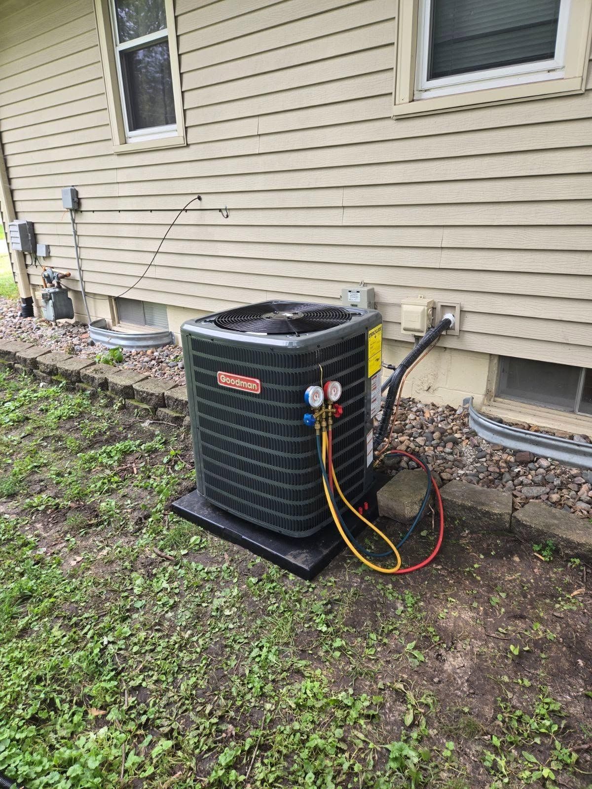 Outdoor air conditioner unit beside a beige house, with hoses and wiring attached.