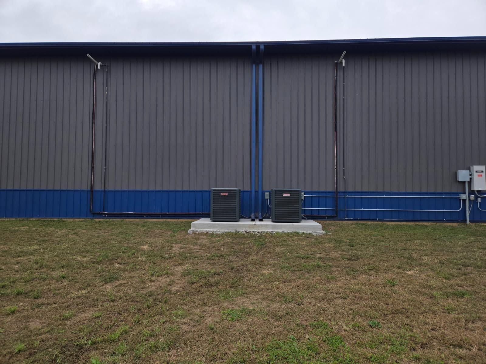 Blue industrial building with a small concrete pad, pipes, and grass in front