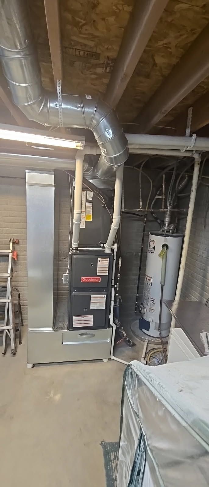 Basement utility room with furnace, ducts, water heater, and exposed joists above concrete floor.