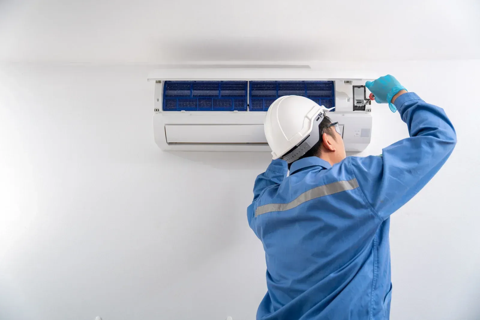 Technician in blue uniform cleaning a wall-mounted air conditioner with a spray bottle and cloth