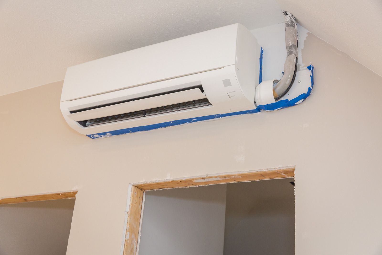 Wall-mounted white air conditioner above a doorway, with exposed blue wiring on the right side
