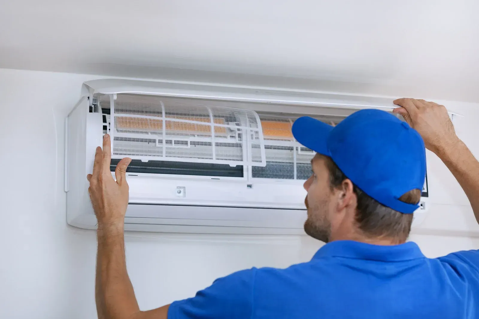 Technician installing a white wall-mounted air conditioner with a blue cap on.