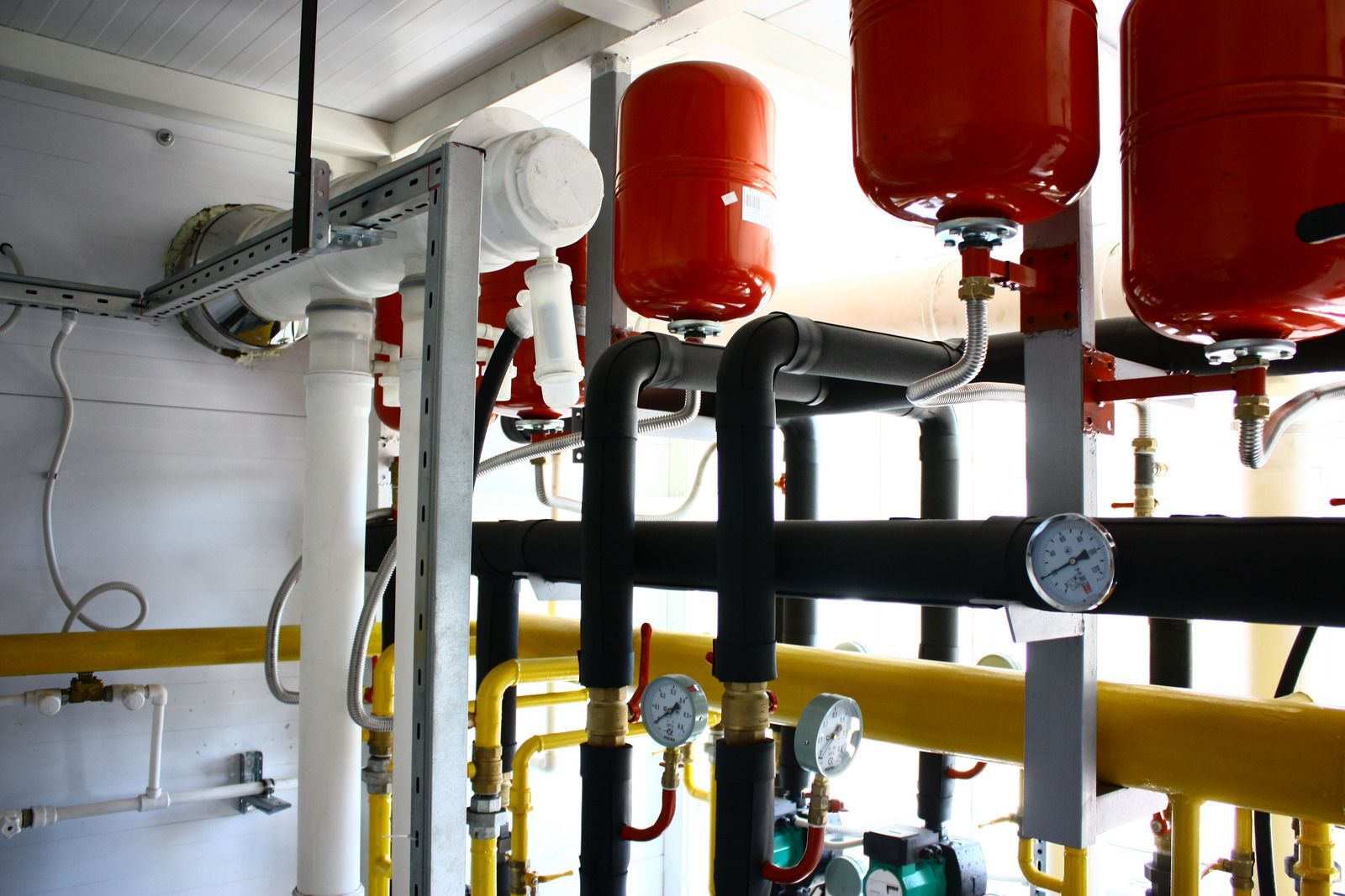 Industrial piping with red tanks and yellow pipes in a mechanical room