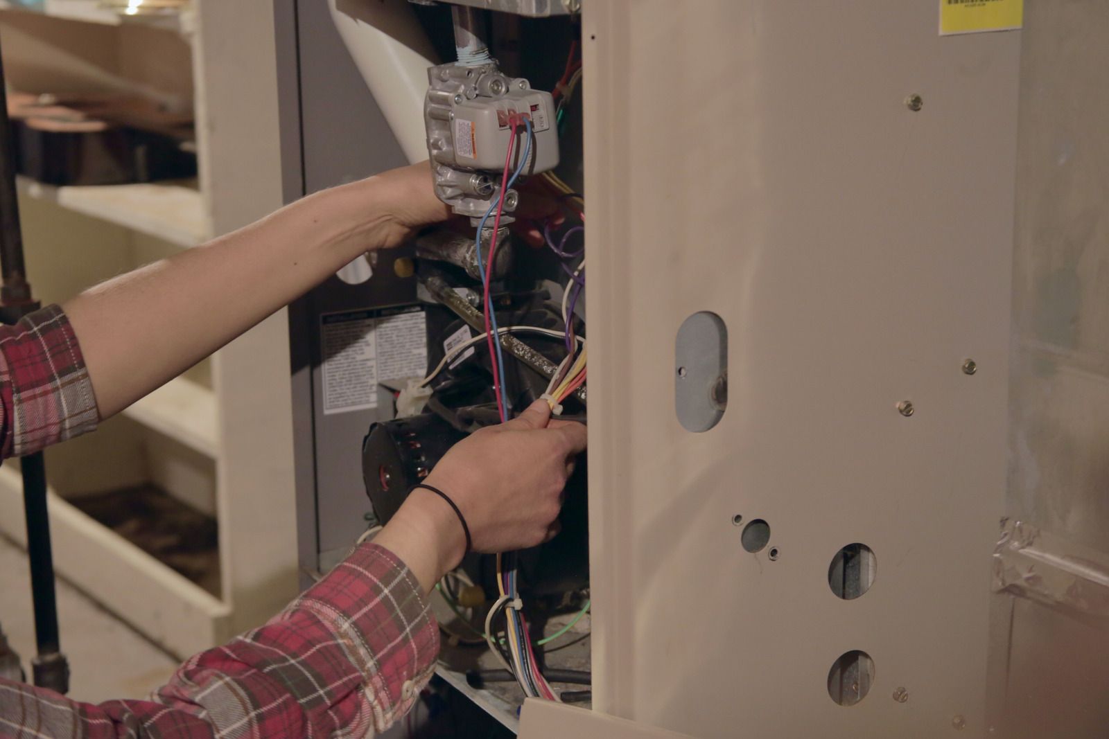 Technician wiring an open electrical panel inside a cabinet, with cables and components exposed.