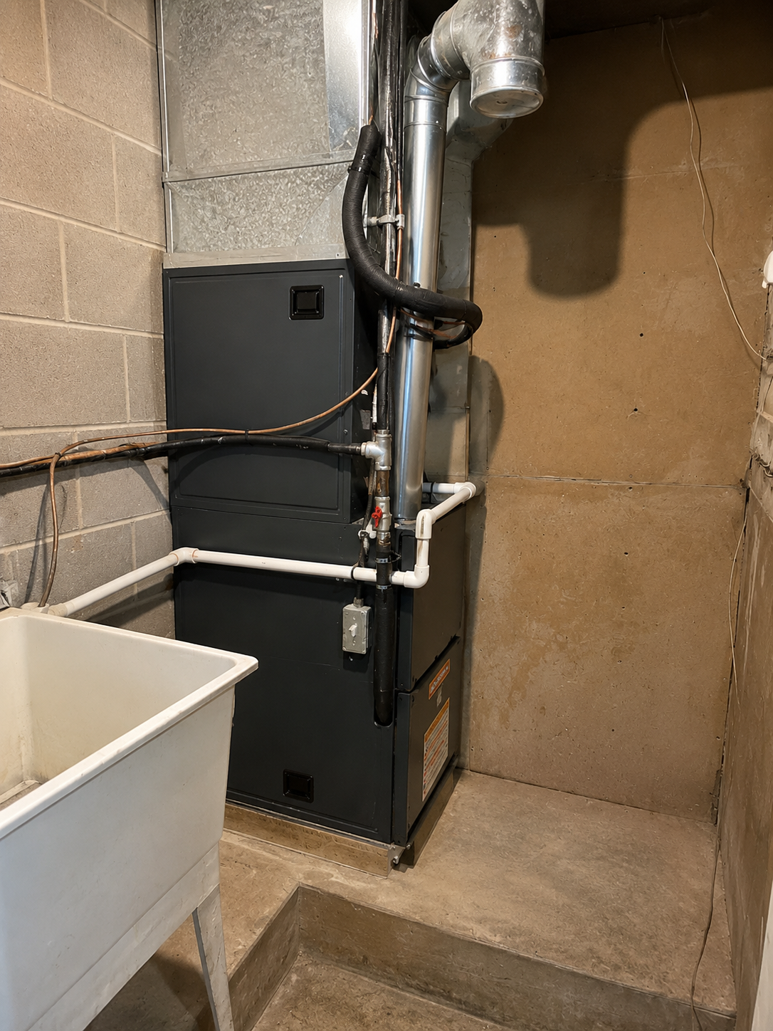 Basement utility area with stacked black HVAC units, exposed ducts, and a utility sink