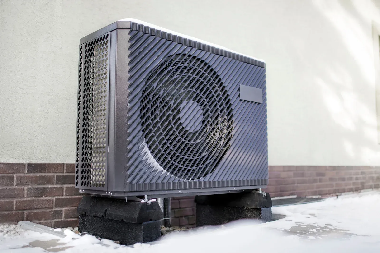 Outdoor HVAC unit with a large fan, set on a snowy ground beside a building wall