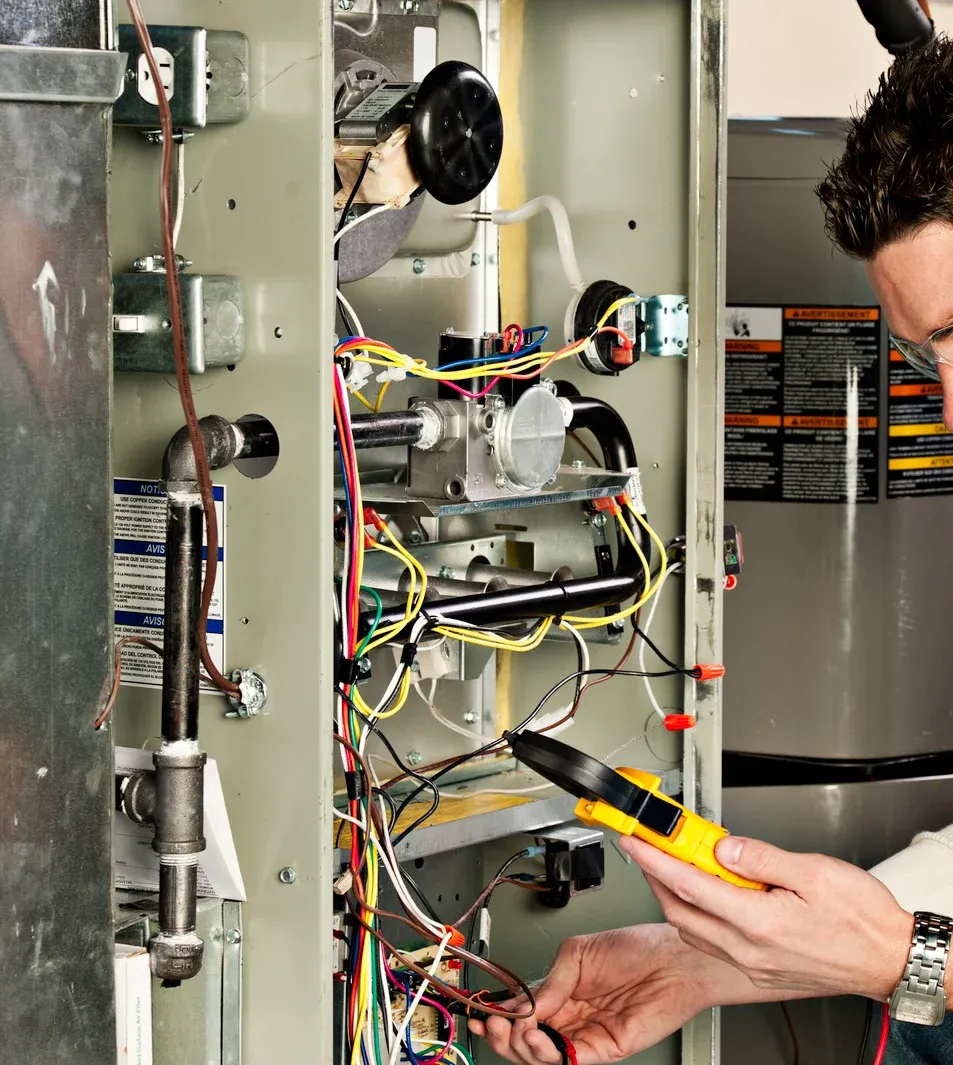Technician wiring an open electrical panel with a yellow multimeter probe in a utility room