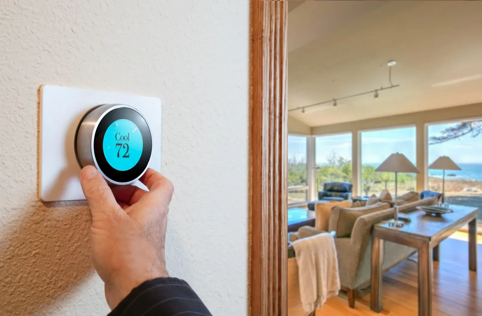 Hand adjusting a smart thermostat in a bright home with a dining area and windows in view