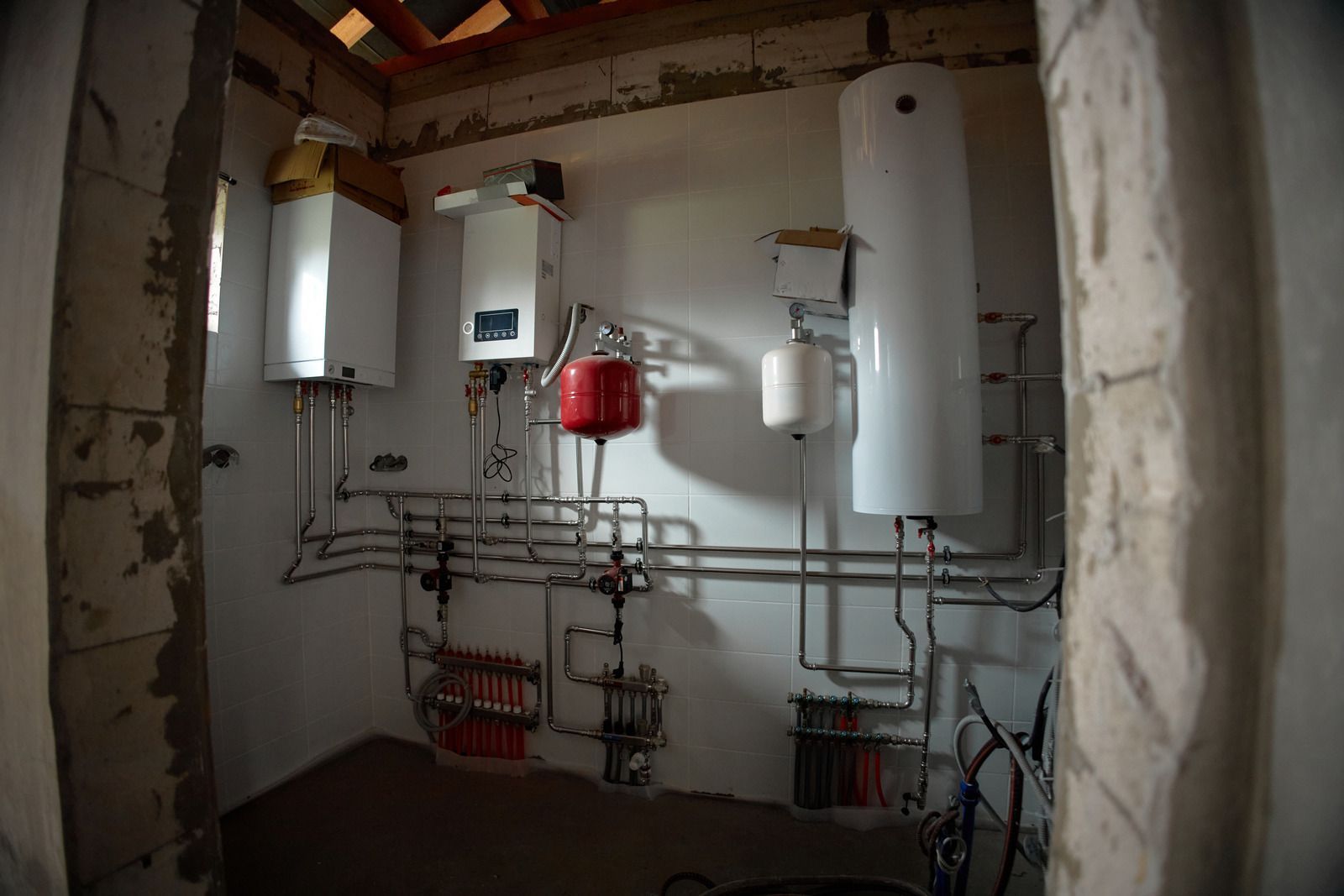 Boiler room with wall-mounted water heaters, pipes, and a red pressure tank in a white utility space