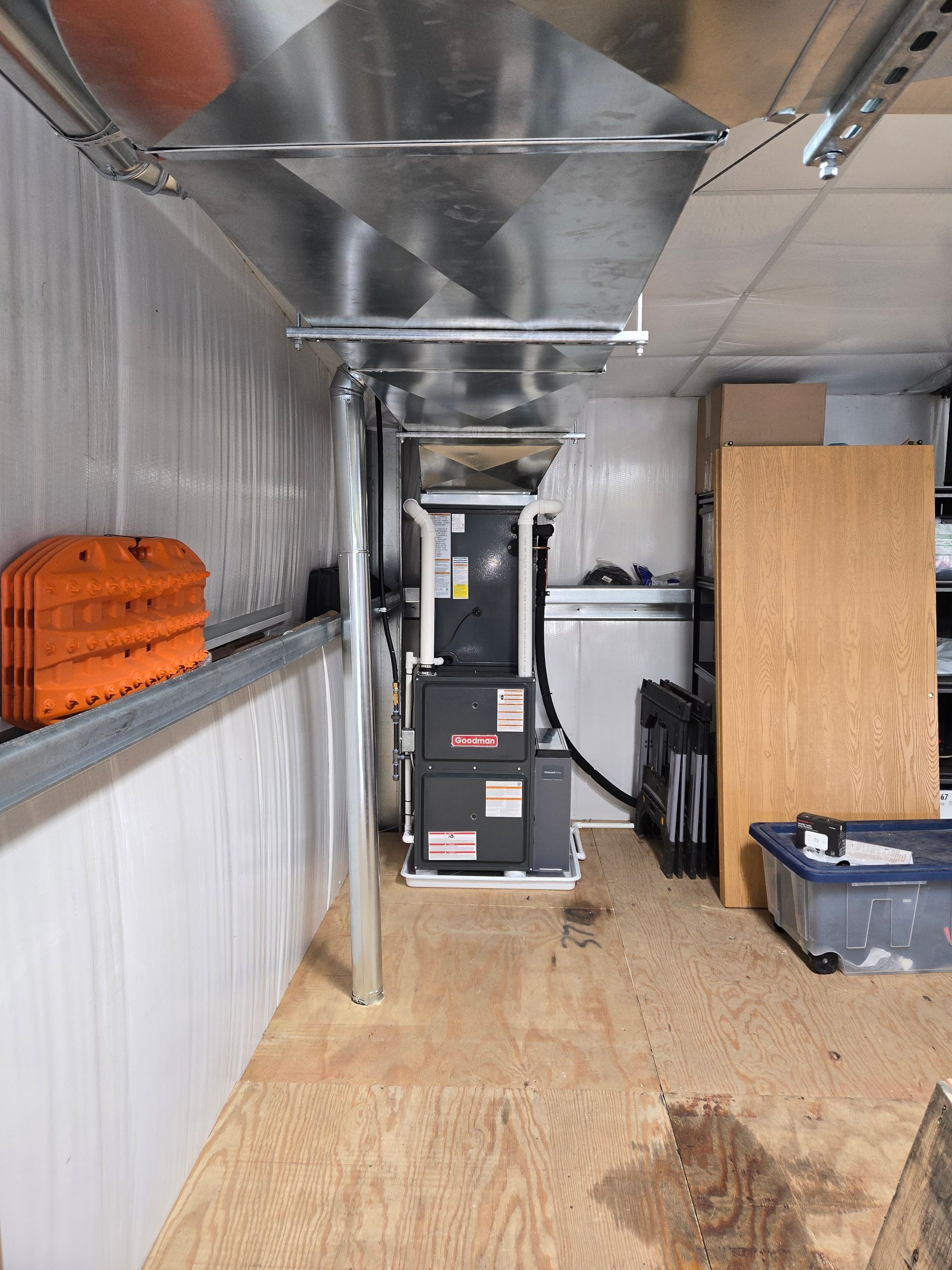 Indoor utility room with metal ductwork, a furnace, plywood floor, and stored bins along the walls