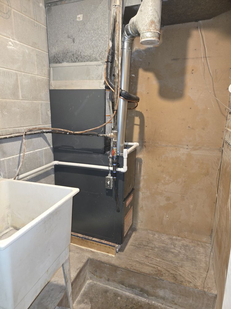 Basement utility room with black tank, pipes, and a white sink basin against concrete walls.