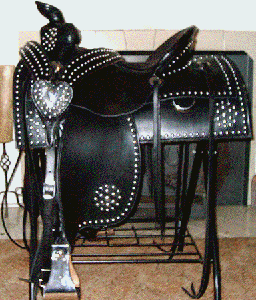 Black studded western saddle on a black metal stand. Heart-shaped concho. Fireplace in the background.