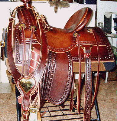 Brown leather Western saddle with decorative tooling, gold accents, on a display stand.