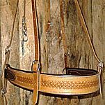 Leather horse breast collar with decorative tooling, tan and brown, hanging against a wooden backdrop.