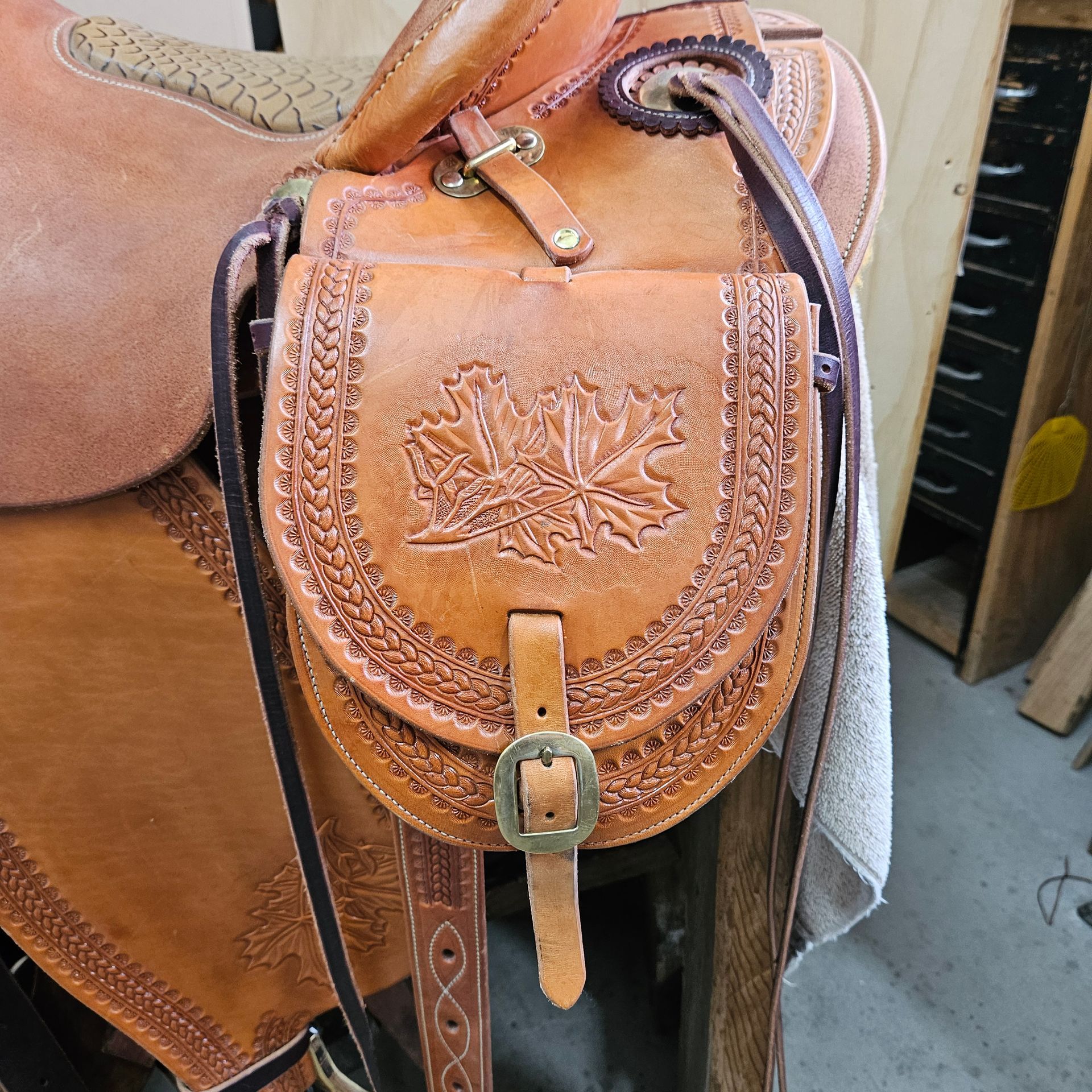 Brown leather saddle bag with basket weave design and floral emblem.