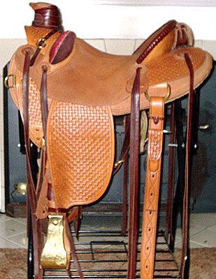 Brown leather Western saddle on a black metal stand, near a fireplace.