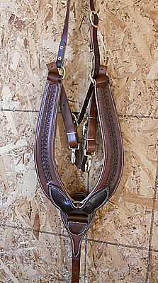 Brown leather horse breast collar with tooling, hanging against a wood wall.
