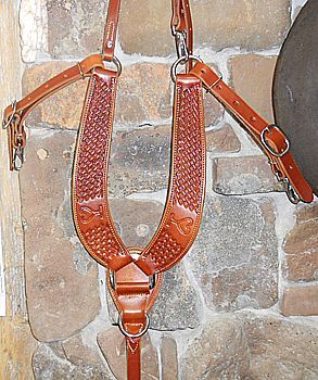 Brown leather horse breast collar with tooled pattern and straps against stone wall.