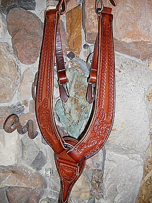 Brown leather horse breast collar with floral tooling, hanging on a stone wall.