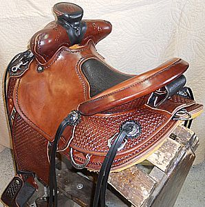 Brown leather western saddle with intricate tooling, on a wooden stand.