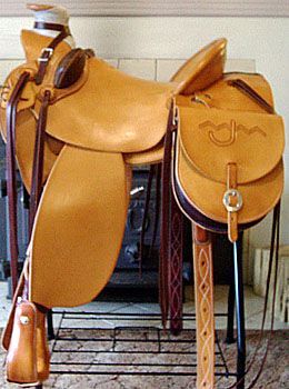 Tan leather western saddle with tooling, on a stand.