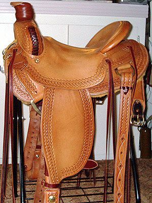 Tan leather western saddle with detailed tooling, stirrups, and tack.