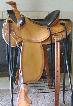 Tan leather western saddle on a black metal stand; black seat and stirrups.
