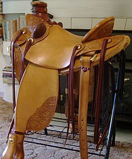 Tan leather western saddle with tooled design on a black metal stand.