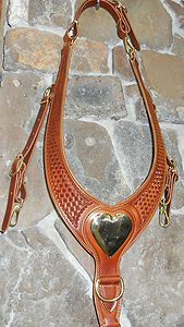 Leather horse breast collar with heart-shaped brass plate, hanging against a stone wall.